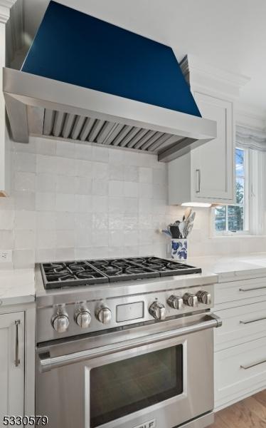 kitchen featuring high end range, white cabinetry, tasteful backsplash, and range hood