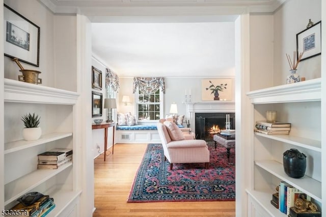 sitting room with wood-type flooring, built in features, and crown molding