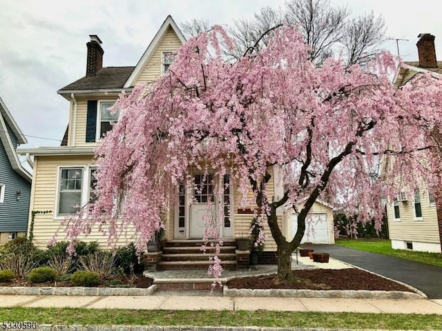 obstructed view of property featuring an outdoor structure, a garage, driveway, and a chimney