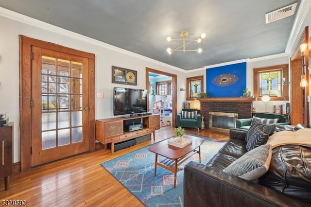 living room with visible vents, wood finished floors, an inviting chandelier, a fireplace, and crown molding