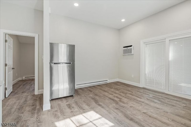 unfurnished room featuring light wood-type flooring, a wall unit AC, and a baseboard radiator