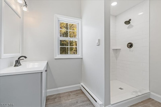 bathroom featuring hardwood / wood-style floors, vanity, tiled shower, and a baseboard heating unit