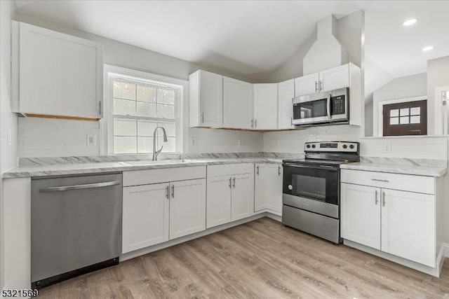 kitchen with sink, vaulted ceiling, decorative backsplash, white cabinetry, and stainless steel appliances