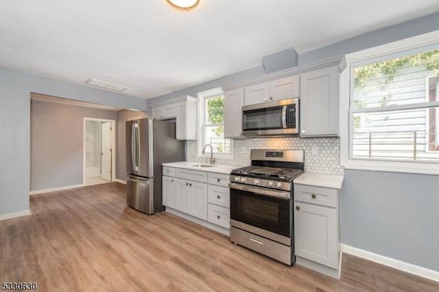 kitchen with appliances with stainless steel finishes, tasteful backsplash, sink, light hardwood / wood-style flooring, and white cabinets