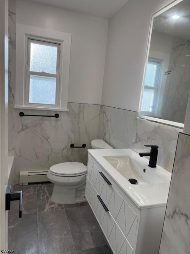 bathroom with vanity, toilet, baseboard heating, and tile walls