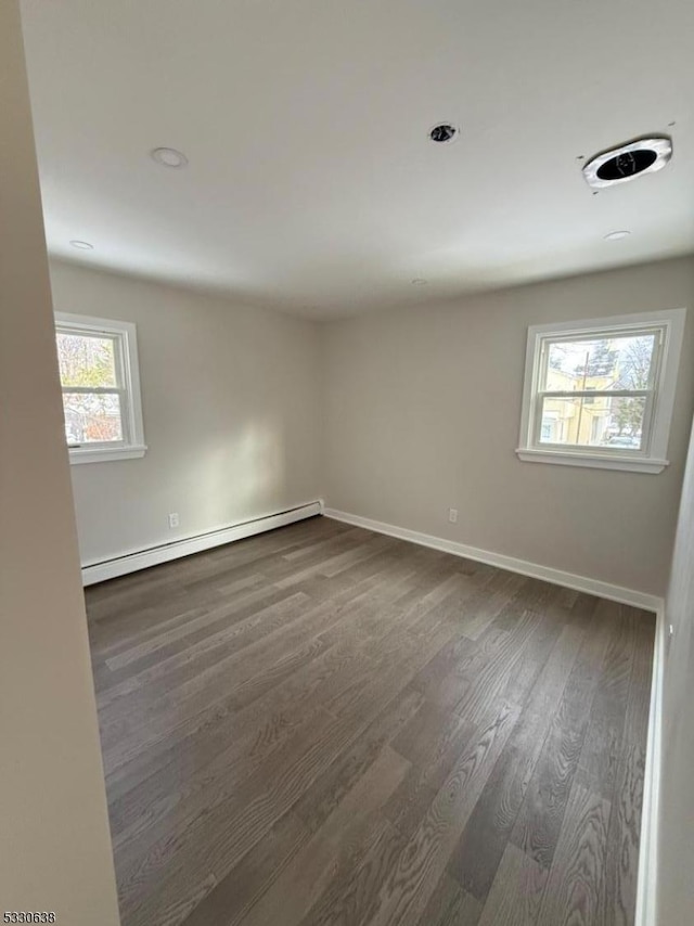 spare room featuring dark hardwood / wood-style flooring, baseboard heating, and a wealth of natural light