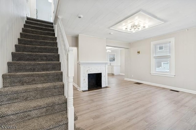 staircase featuring a fireplace with flush hearth, wood finished floors, visible vents, and baseboards