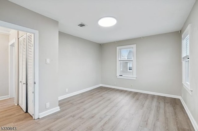 empty room with wood finished floors, visible vents, and baseboards