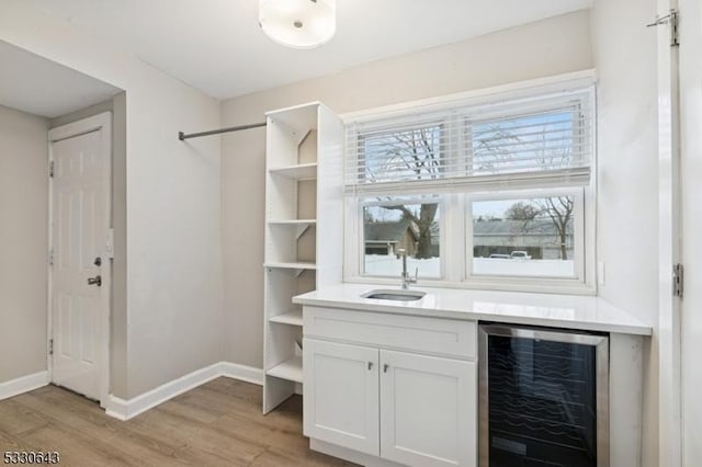 bar with light wood-type flooring, wine cooler, baseboards, and a sink