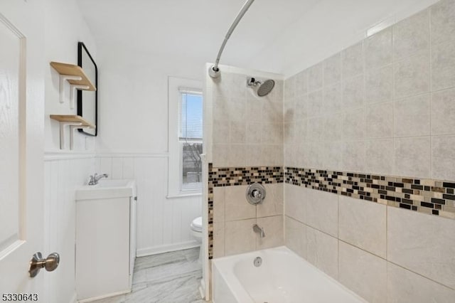 bathroom with marble finish floor, shower / bath combination, toilet, wainscoting, and a sink