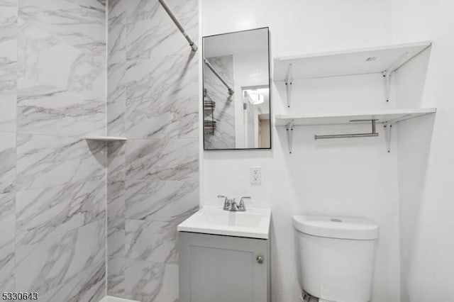 bathroom with toilet, tiled shower, and vanity