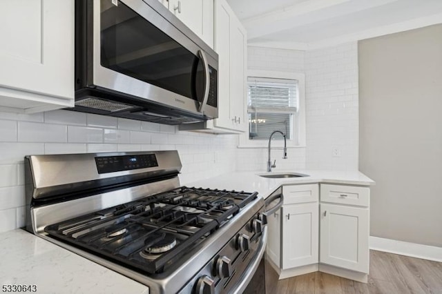 kitchen with appliances with stainless steel finishes, a sink, white cabinetry, and decorative backsplash