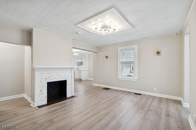 unfurnished living room with light wood finished floors, a fireplace with flush hearth, visible vents, and a notable chandelier