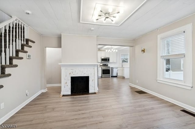 unfurnished living room featuring visible vents, a fireplace with flush hearth, a chandelier, light wood-type flooring, and stairs