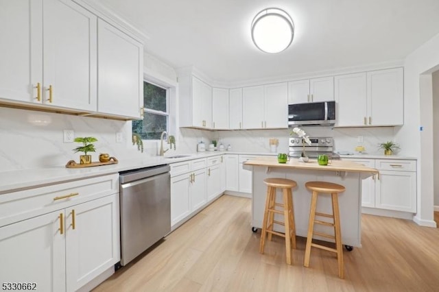 kitchen with a kitchen island, a breakfast bar area, appliances with stainless steel finishes, white cabinetry, and a sink