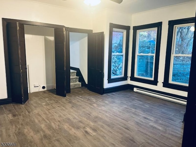 empty room featuring ceiling fan, dark hardwood / wood-style flooring, and a baseboard heating unit