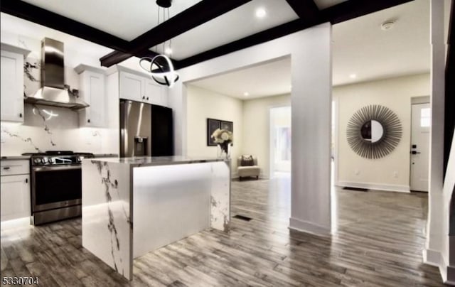 kitchen with dark wood-type flooring, appliances with stainless steel finishes, a kitchen island, wall chimney range hood, and white cabinets