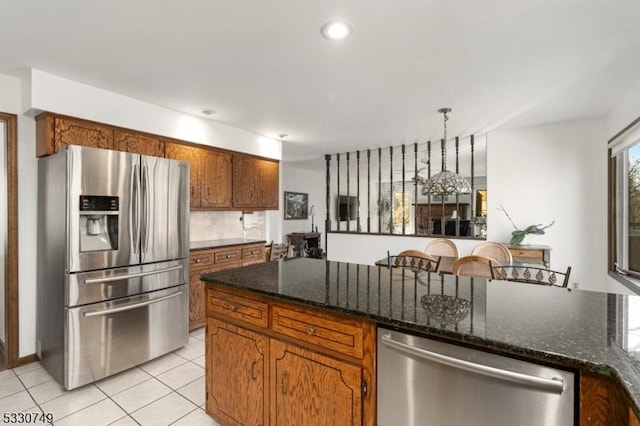 kitchen with hanging light fixtures, dark stone countertops, decorative backsplash, light tile patterned floors, and appliances with stainless steel finishes