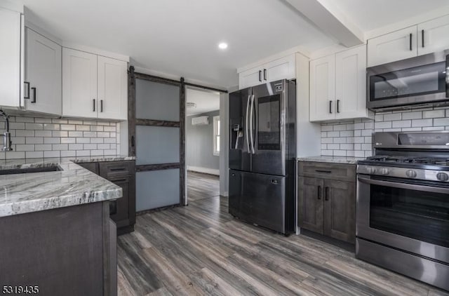 kitchen with appliances with stainless steel finishes, light stone counters, sink, a barn door, and white cabinets