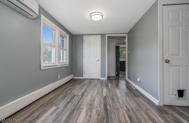 unfurnished bedroom with baseboard heating, a wall unit AC, and dark wood-type flooring