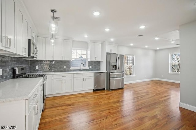 kitchen featuring pendant lighting, light hardwood / wood-style floors, white cabinetry, and appliances with stainless steel finishes