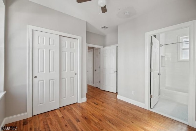 unfurnished bedroom featuring ensuite bath, ceiling fan, light wood-type flooring, and a closet