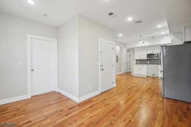 kitchen with tasteful backsplash, white cabinets, stainless steel appliances, and light hardwood / wood-style flooring