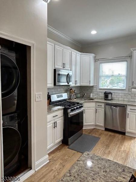 kitchen with white cabinets, appliances with stainless steel finishes, stacked washer and dryer, and tasteful backsplash