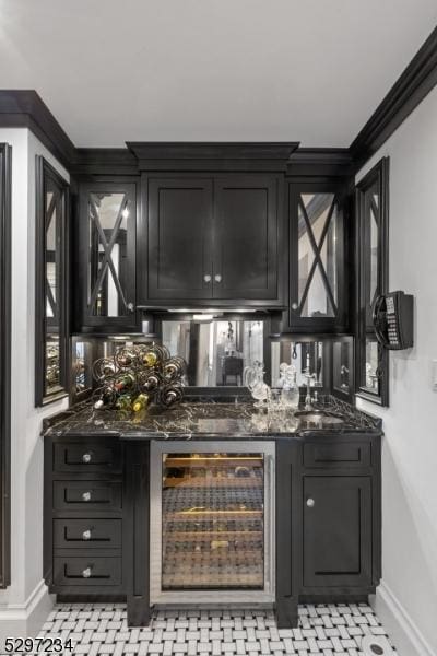 bar featuring sink, wine cooler, ornamental molding, and dark stone countertops