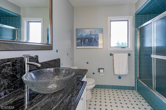 full bathroom featuring vanity, toilet, a healthy amount of sunlight, and enclosed tub / shower combo