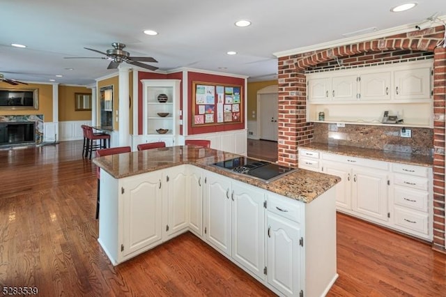 kitchen featuring black electric stovetop, ornamental molding, hardwood / wood-style flooring, dark stone countertops, and white cabinetry