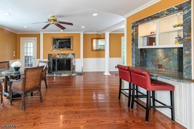 dining area featuring ornate columns, ceiling fan, crown molding, and a premium fireplace