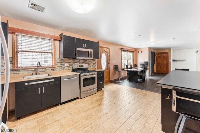 kitchen with tasteful backsplash, sink, light hardwood / wood-style floors, and appliances with stainless steel finishes