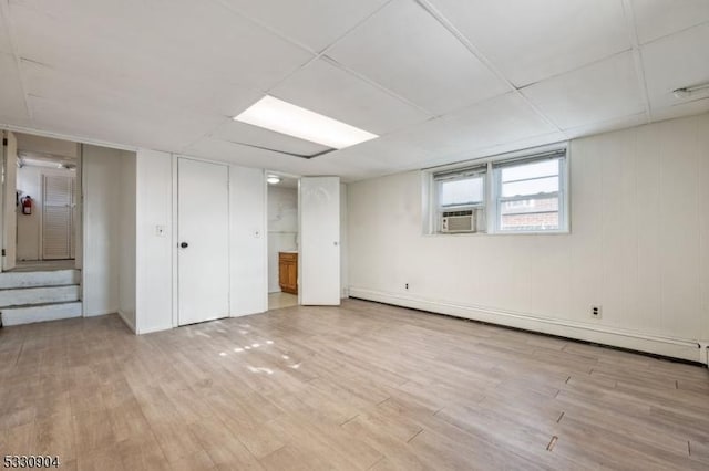 basement with a paneled ceiling, cooling unit, light hardwood / wood-style flooring, and a baseboard radiator