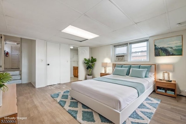 bedroom with light wood-type flooring, ensuite bath, a drop ceiling, and cooling unit