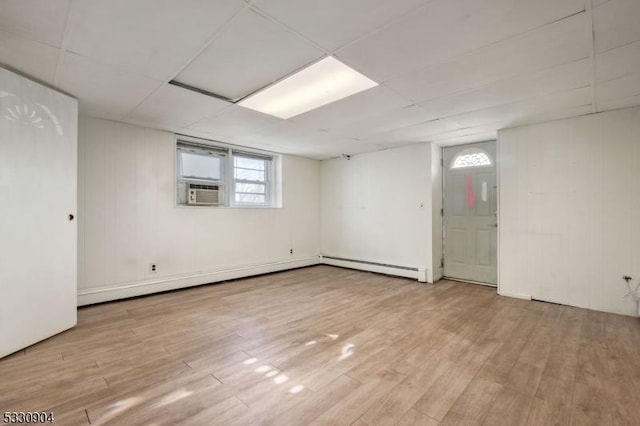 basement featuring a paneled ceiling, light hardwood / wood-style flooring, baseboard heating, and cooling unit