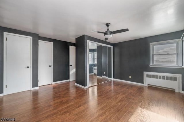 unfurnished bedroom with radiator, ceiling fan, hardwood / wood-style floors, and multiple closets