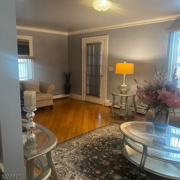 living room with hardwood / wood-style floors, a baseboard heating unit, and crown molding