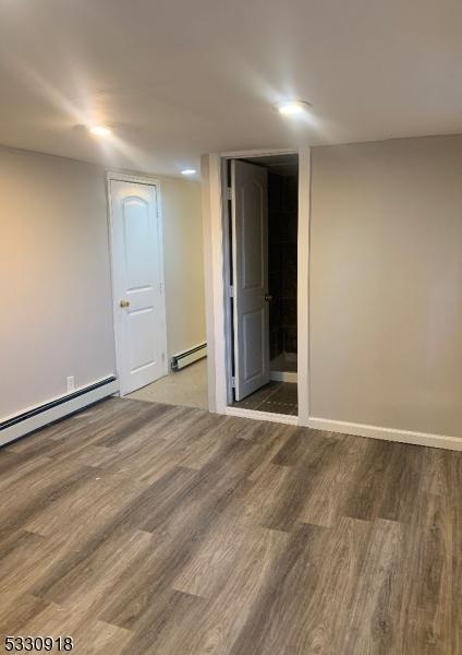 unfurnished room featuring a baseboard heating unit and hardwood / wood-style floors