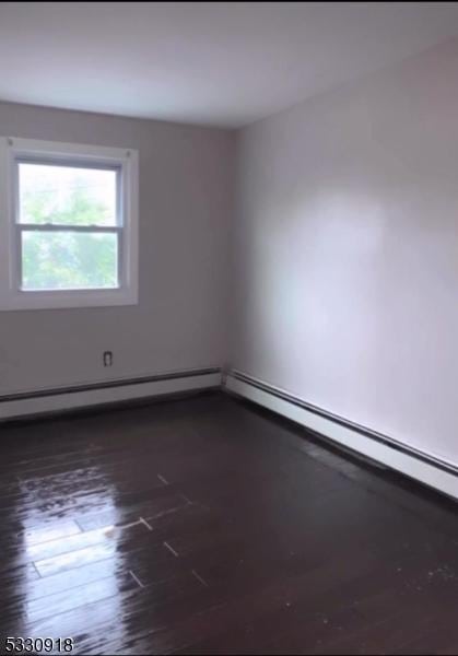 spare room featuring baseboard heating and dark wood-type flooring