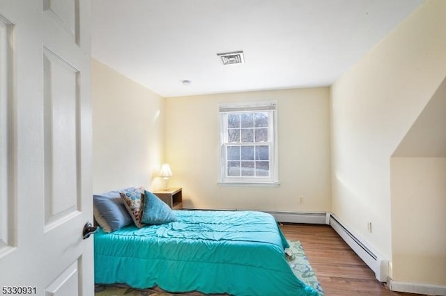 bedroom with wood-type flooring and a baseboard heating unit