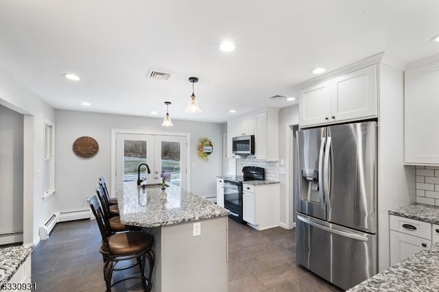 kitchen featuring a center island with sink, light stone counters, white cabinetry, and appliances with stainless steel finishes