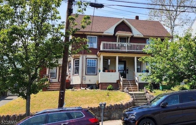 view of front of house with covered porch, a balcony, and a front lawn