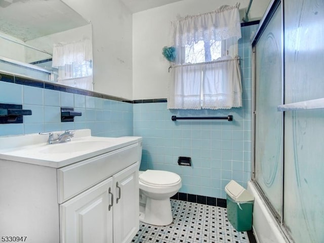 full bathroom featuring shower / bath combination with glass door, vanity, tile walls, and toilet