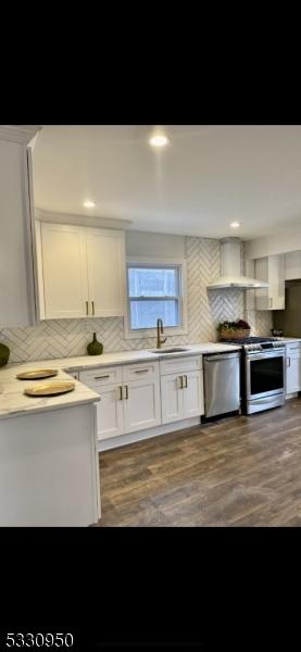 kitchen with white cabinetry, sink, wall chimney exhaust hood, stainless steel appliances, and backsplash