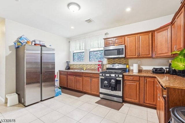 kitchen with tasteful backsplash, sink, light stone countertops, appliances with stainless steel finishes, and light tile patterned floors