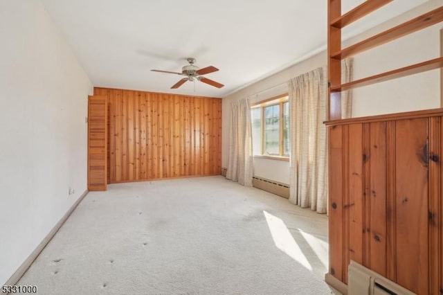 carpeted spare room with ceiling fan, wooden walls, and a baseboard radiator