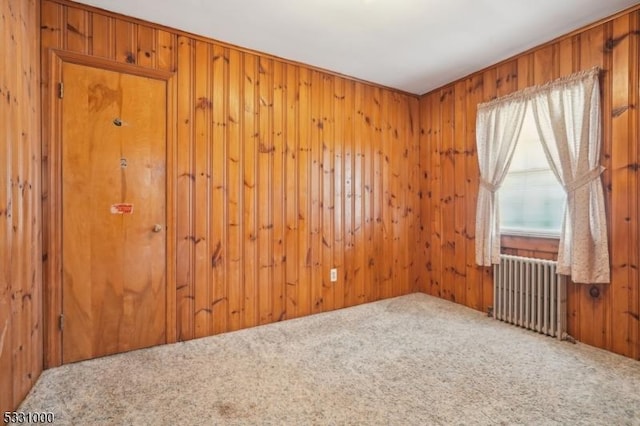 unfurnished room with carpet floors, wooden walls, and radiator