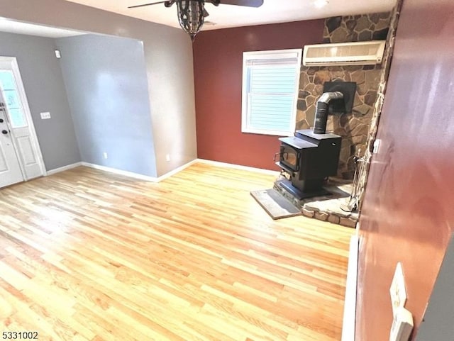 living room featuring wood-type flooring, a wood stove, ceiling fan, and an AC wall unit