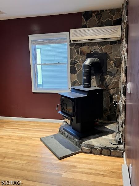 room details with a wall unit AC, a wood stove, and hardwood / wood-style flooring